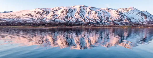 The Lyngen Alps are reflected in the light of the midnight sun in Sør-Lenangen Bay